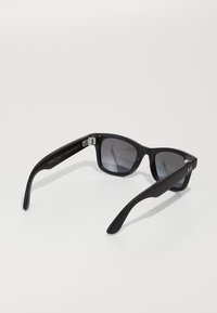 Schwarze Kunststoff-Sonnenbrille mit dunklen, verlaufenden Gläsern, quadratischen Rahmen und matter Oberfläche. Verfügt über ein silbernes Logo am Bügel und metallische Scharnierakzente.