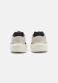 Zapatillas deportivas con parte superior de malla negra y gris, con una gruesa entresuela blanca y suela de goma texturizada. Detalles notables del logo de las tres rayas.