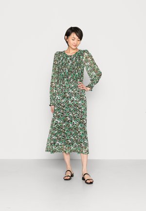 Vestido longo floral com um padrão verde, preto e branco. Apresenta mangas longas transparentes e um decote franzido, caindo abaixo do joelho.