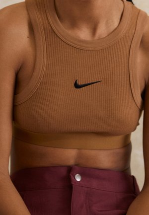 Osoba nosząca brązowy prążkowany krótki top z czarnym logo Nike i bordowe spodnie z wysokim stanem oraz srebrnym guzikiem.