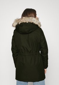 Veste parka verte avec une capuche doublée en fausse fourrure, taille cintrée et manches longues, présentant une texture lisse et un design décontracté.