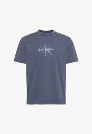 T-shirt bleu à manches courtes et col rond avec un grand logo texte "cK" gris clair et "Calvin Klein" blanc centré sur le devant.