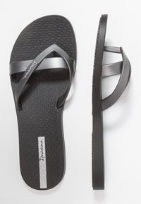 Schwarze Flip-Flops mit strukturierten Sohlen, die breite matte Riemen haben. Die Marke "Ipanema" ist auf einem silbernen Akzent an der Sohle sichtbar.