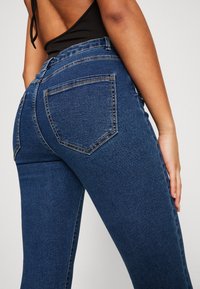 Mörkblå, högmidjade jeans i denim med en figursydd design, som har två bakfickor och stickade detaljer.