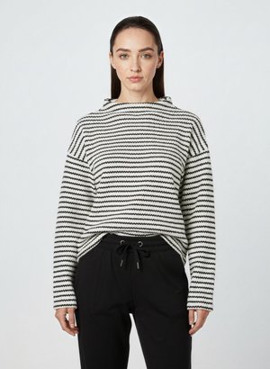 Pull à rayures noir et blanc avec un col haut, coupe ample et motif de tricot texturé, associé à un pantalon noir avec cordon de serrage.