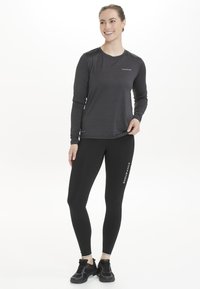 Langærmet mørkegrå træningsshirt parret med sorte leggings, der har hvid "ENDURANCE" tekst langs siden, og sorte sneakers.