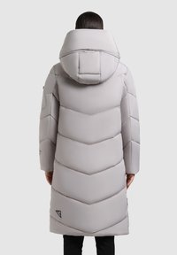 Abrigo acolchado gris claro con un patrón de rombos, capucha de gran tamaño y bolsillos laterales. Tejido texturizado y detalle del logo cerca del dobladillo.