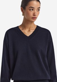 Marinblå V-ringad tröja med lös passform, ribbad halsringning och mjuk yta. Tyget verkar lätt och något fluffigt.