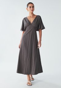 Maxikjole i mørkegråt stof med hvide polkaprikker, V-hals og korte flagrende ærmer, med en afslappet pasform og flydende design.