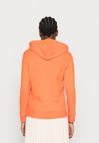 Sudadera naranja hecha de una tela suave, con capucha ajustable, mangas largas y puños acanalados. El diseño de la parte posterior es liso, sin adornos.