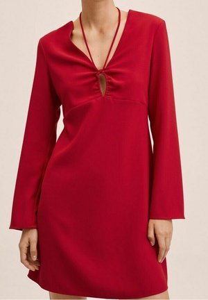 Femme portant une robe rouge à manches longues avec un décolleté en forme de trou de serrure froncé au niveau de la poitrine et une coupe ample au-dessus des genoux.