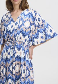 Robe à motifs bleus et blancs avec des manches courtes et larges, un col en V et un cordon ajustable à la taille. Tissu léger.