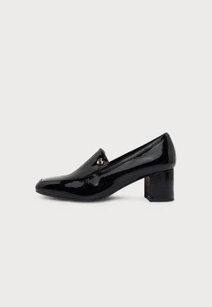 Mocassin noir en cuir verni avec un petit ornement doré et un talon bloc épais, présenté de profil sur un fond clair.