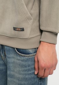 Fleece genser i grått med kengurulomme, ribbede mansjetter og et merke med koordinater. Kombinert med blå denim jeans.