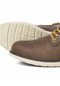 Des chaussures en cuir marron avec un bout arrondi, une semelle claire contrastante et des lacets jaunes. La semelle présente un motif de grip texturé.