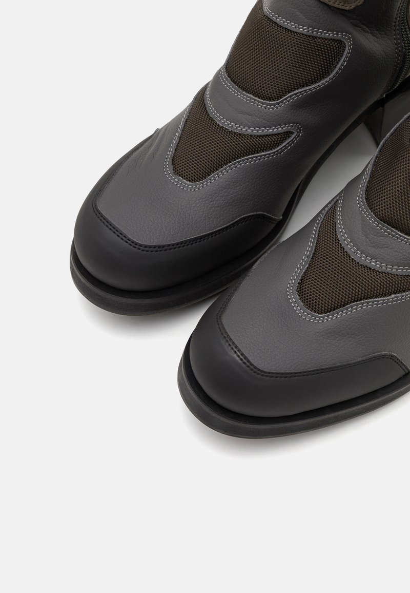 Grijze leren laarzen met gaaspanelen, ronde neuzen en contrasterende zwarte zolen. Gedetailleerde stiksels en gladde texturen verbeteren het ontwerp.