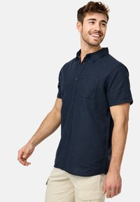 Camisa de manga corta azul marino hecha de un tejido ligero con botón en el frente, bolsillo en el pecho y un cuello estructurado; ajuste casual con detalles cosidos.