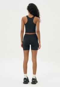 Zwarte sportieve tanktop en shorts van rekbaar materiaal, met een fitted ontwerp en naadloze constructie. Gekleed met zwarte sneakers.