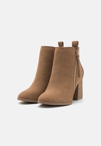 Brown suede ankle boots with a pointed toe, side zipper, and a chunky textured heel. Features a pull tab on the back for easy wear.