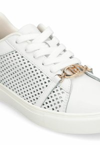 Baskets blanches avec côtés en mesh, lacets plats, et un accent logo ton or. Cuir lisse et tissu texturé créent un design visuel contrasté.