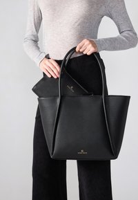 Svart texturerad tygväska med dubbla handtag och en mindre zip-väska inuti. Logotypen präglad i guld på framsidan.