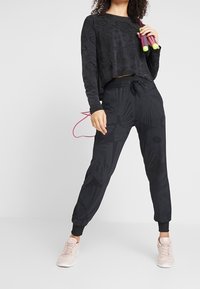 Black cropped long-sleeve top with textured pattern, paired with black joggers featuring a floral design, completed with light pink athletic shoes.