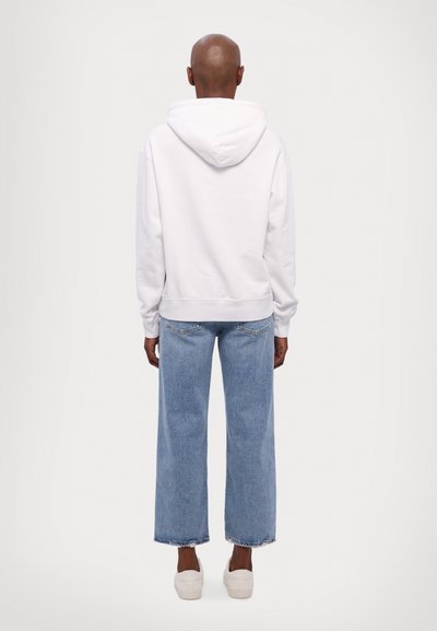 White hooded sweatshirt with ribbed cuffs and hem, paired with light blue wide-leg jeans featuring a frayed hem, worn with beige slip-on shoes.