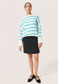 Gestreifter Strickpullover in Creme und Aqua, mit einem lässigen Schnitt und tiefen Schultern, kombiniert mit einem schwarzen, figurbetonten Rock und schwarzen Ballerinas.