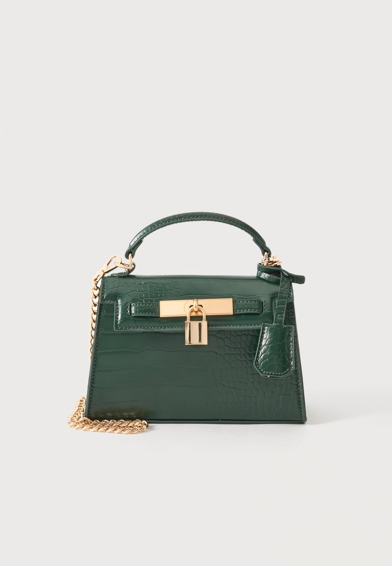 Sac à main vert foncé avec texture crocodile, poignée supérieure, détail de serrure dorée et bandoulière chaîne dorée amovible sur un fond clair uni.