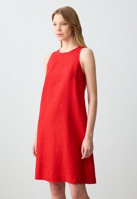 Rotes ärmelloses Leinenkleid mit einem runden Ausschnitt. Der Stoff hat eine dezente Textur und fällt sanft bis zur Mitte des Oberschenkels in einer A-Linie.