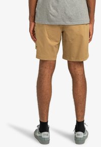 Khaki shorts with side pockets and stitched detailing, paired with gray socks and light blue sneakers featuring a logo on the heel.