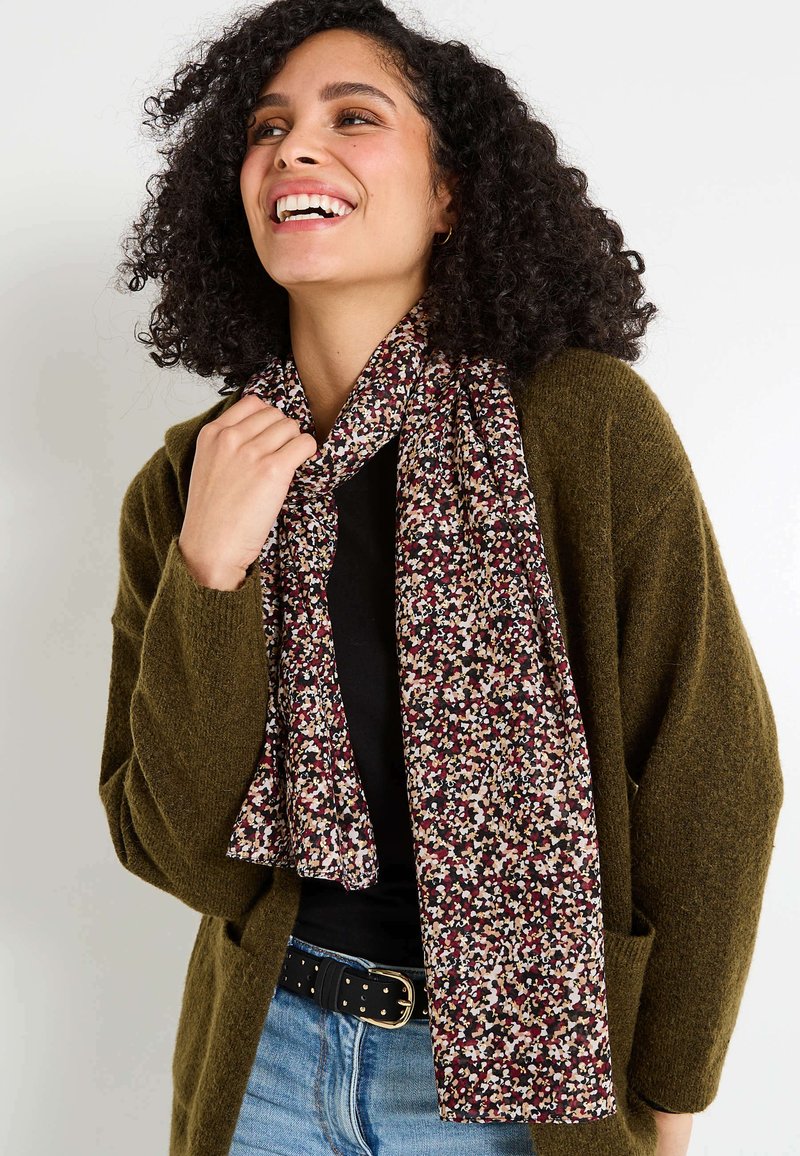 Bufanda con estampado floral hecha de una tela suave en color burdeos, crema y azul oscuro. Lleva puesta de forma suelta con un cárdigan texturizado verde, sin herrajes visibles.