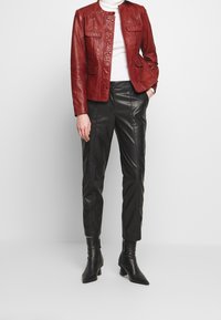 Röd läderjacka med rund krage, tryckknappar och två framfickor. Kombinerad med svarta läderbyxor som är smalnande och spetsiga ankelstövlar.