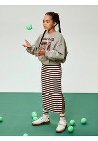 Szara bluza z napisem "GIRLS CLUB 91" w ciemnoczerwonym kolorze, brązowo-biała spódnica w paski, białe tenisówki na tle zielonego tła z piłkami tenisowymi.