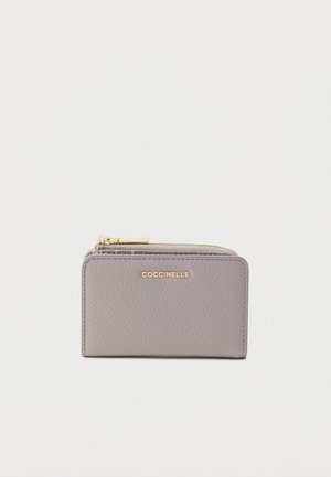 Grijze leren portemonnee met een gestructureerde afwerking, voorzien van een gouden logo en ritssluiting. Compacte rechthoekige vorm met strakke lijnen.