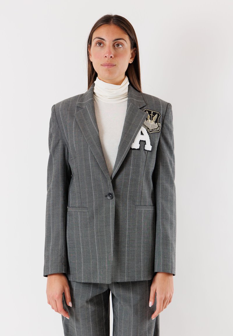 Blazer grigio a righe sottili su misura con due tasche, chiusura a un bottone e un patch ricamato con una "A" sul lato sinistro del petto.