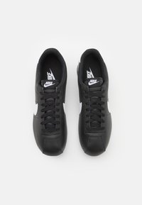 Sneakeri negri Nike cu un superior din piele netedă, swoosh alb, șirete negre și guler căptușit. Insolă texturată și talpă plată din cauciuc.