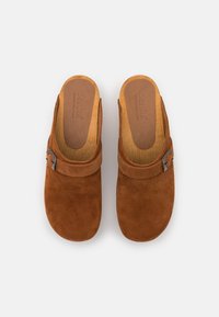 Zoccoli in suede marrone senza laccio con soletta in cuoio, una fascia sopra il collo del piede e un accento in metallo a forma di fibbia di lato.