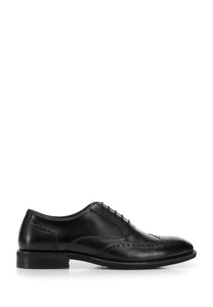 Scarpa elegante da uomo in pelle nera con dettagli brogue e allacciatura chiusa, mostrata di profilo su sfondo bianco.