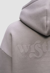Felpa con cappuccio in tessuto grigio chiaro con stampa del logo testurizzata. Presenta un design rilassato e cuciture visibili sulle cuciture.