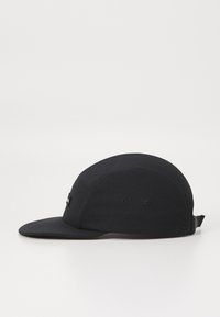 Svart caps med buet skygge, laget av stoff, med flate sømmer, ventilasjonsventiler og en justerbar stropp bak.