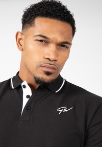 Zwarte polo met witte accenten, voorzien van een twee-knopen knoopsluiting en een geborduurd logo op de borst. Getextureerde stof en een getailleerde pasvorm.