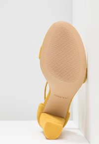 Sandale jaune à talon reposant sur son talon, semelle tournée vers l'avant montrant la marque ALDO et un motif de grip texturé.