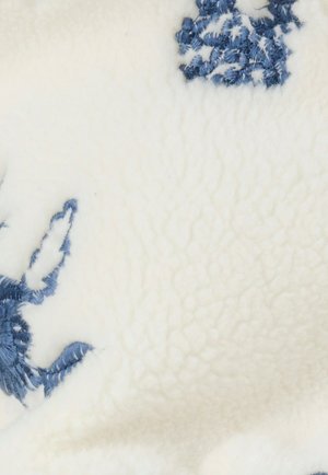 Weiche Fleece-Decke in Weiß mit blauen, bestickten Blumenmustern. Verfügt über eine strukturierte Oberfläche, die feine Stickdetails hervorhebt.