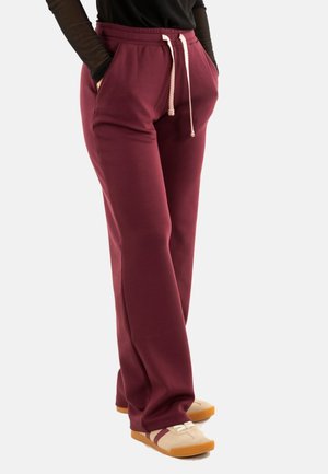 Pantalons de survêtement bordeaux avec un cordon de serrage, dotés de deux poches latérales et d'une coupe décontractée. Associés à des baskets beiges avec des semelles et des accents marron.