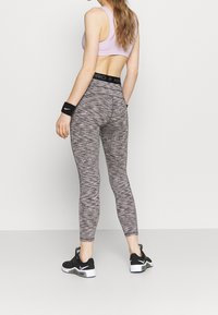 Szare i różowe legginsy melanżowe z wysokim czarnym paskiem. Do tego dopasowany, różowy, krótki sportowy stanik oraz czarne buty sportowe.