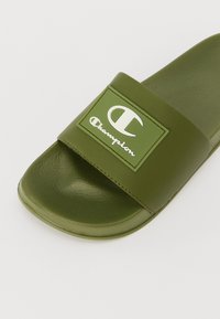 Grønn gummisandal med bred stropp, hevet logopatch, teksturert fotbed og glatt såle.