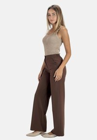 Bruine wijde broek met zijzakken en geplooide voorkant, gecombineerd met een aansluitend beige rib gebreid tanktop en beige ballerina's.