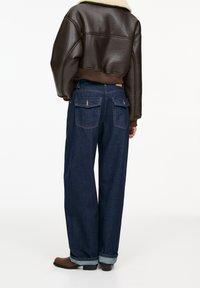 Donkerblauwe wijde jeans met hoge taille, voorzien van twee achterzakken en opgerolde zoom. Gecombineerd met een bruine nep leren cropped jasje.