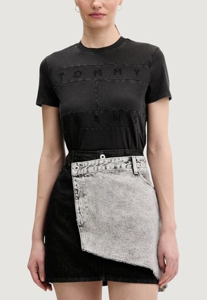 Maglietta nera in cotone con scritte in rilievo "TOMMY" e "JEANS". Abbinata a una gonna in denim nero e grigio, tagliata asimmetricamente con bordi sfrangiati.